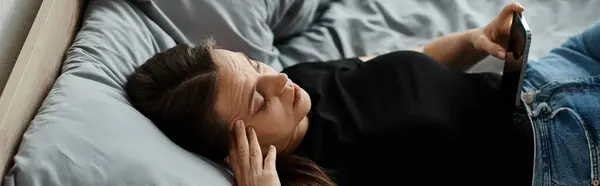 Middle-aged woman laying in bed, holding tablet with a thoughtful expression. — Stock Photo