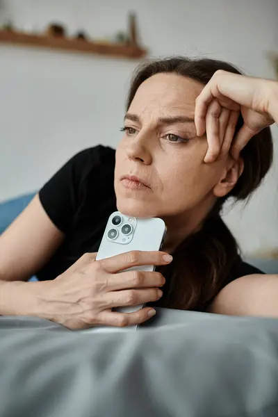 A middle-aged woman lies on a bed holding a phone. — Foto stock