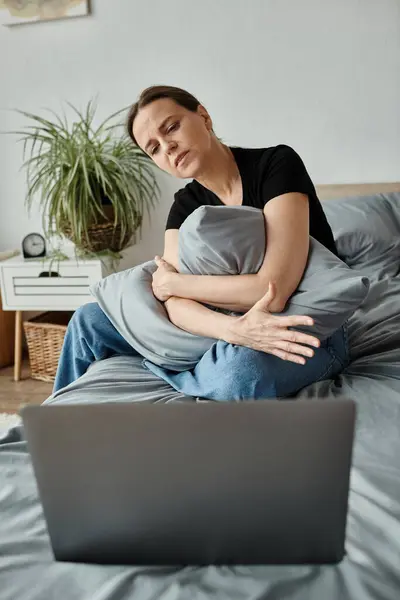 Middle-aged woman sits on bed, engrossed in laptop. — Stock Photo