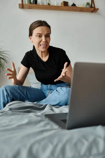 A woman finds solace sitting on a bed with a laptop. - foto de stock