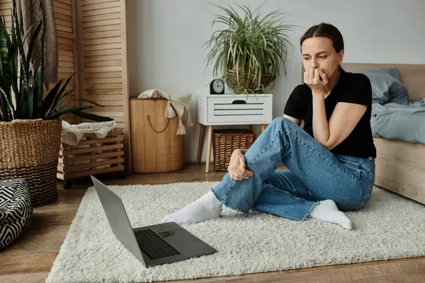 Middle aged woman sitting on floor in front of laptop, immersed in contemplation. — Stock Photo