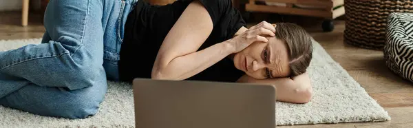 Middle-aged woman lying next to laptop, deep in thought. — Stock Photo