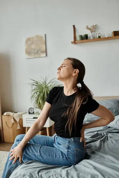 Woman sitting on bed, clutching her back in pain, struggling with depression. — Foto stock