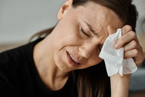 A middle-aged woman wiping her face with a tissue in a moment of vulnerability. — Stockfoto