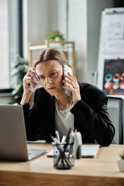 A woman, visibly stressed, talks on the phone while seated at a desk. — Stock Photo