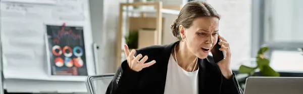 A middle-aged woman talks on the phone, feeling the weight of stress at her office desk. — Stock Photo