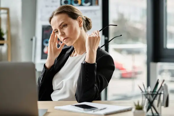 A woman sits at a desk with her eyes closed, finding peace in the midst of stress. — Stock Photo