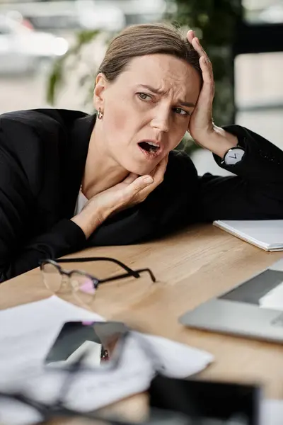 Woman sitting with hands on head, feeling overwhelmed and stressed in office environment. — стокове фото