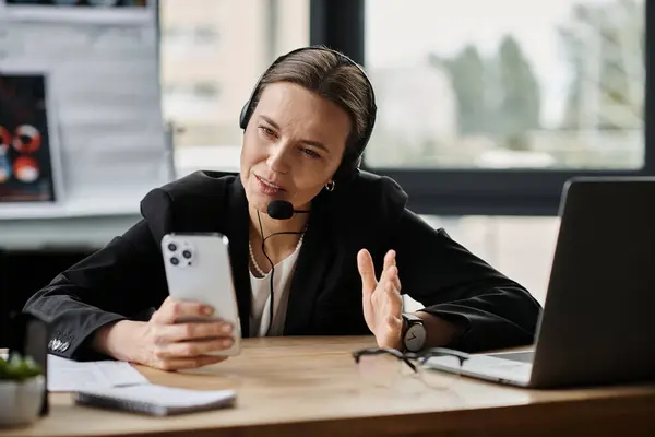 Middle-aged woman in headset having a phone conversation while seated at office desk. — стокове фото