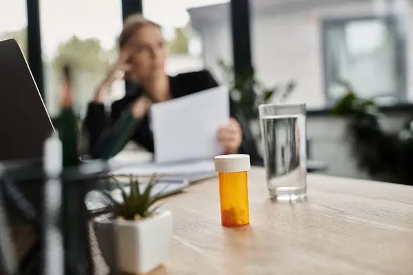 Stressed woman sits at desk with bottle of medicine. — Fotografia de Stock