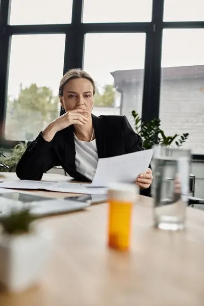 Middle-aged woman sitting at a table, attentively examining a piece of paper. — Stock Photo