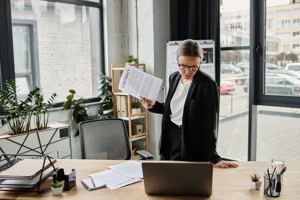 A woman standing stressed at a desk with a document in front of her. — Foto stock