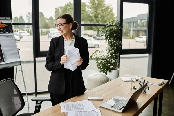 Middle-aged woman in business suit, looking stressed, standing in front of window. — Stock Photo