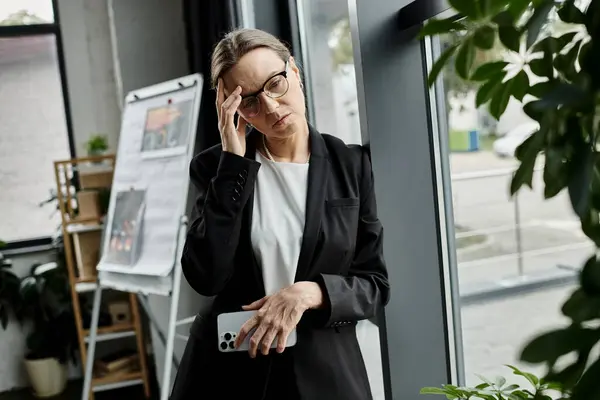 A middle-aged woman in a business suit stands before a plant, her demeanor reflecting stress and melancholy. — Stock Photo