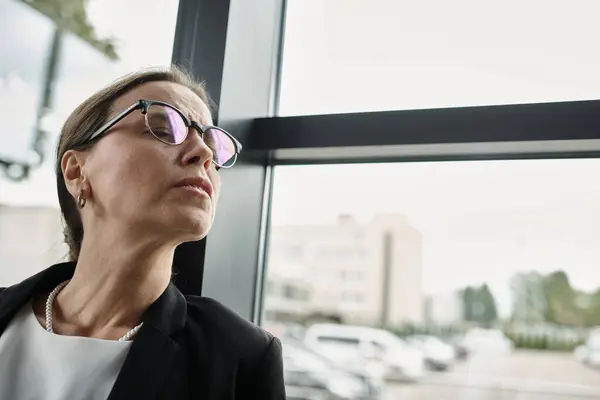 A middle-aged businesswoman in glasses gazes away, depression. - foto de stock