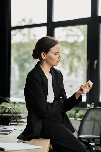 Middle aged woman at desk, staring at pills with a troubled expression. — Fotografia de Stock