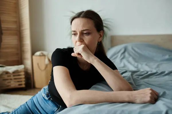 Woman in deep thought, resting on bed with chin on hand. - foto de stock