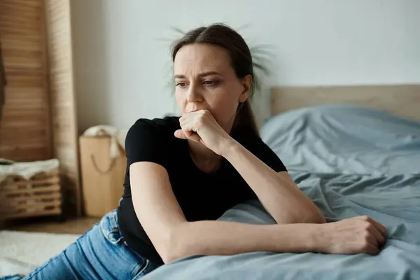 Woman in deep thought, resting on bed with chin on hand. — Fotografia de Stock