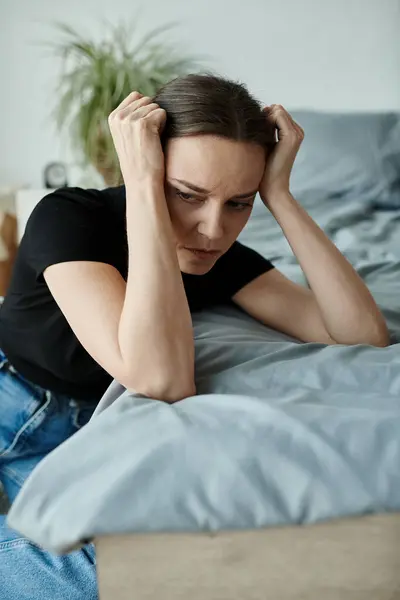 Middle-aged woman in distress lying on bed with hands on head. — Stockfoto