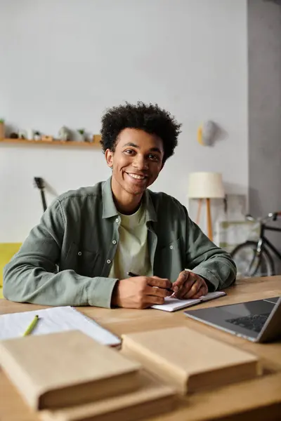 A young man, immersed in his work, sits at a desk with a laptop and a notebook. — Stock Photo