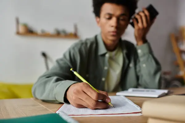 A young African American man sitting at a desk, writing in a notebook. — Stockfoto