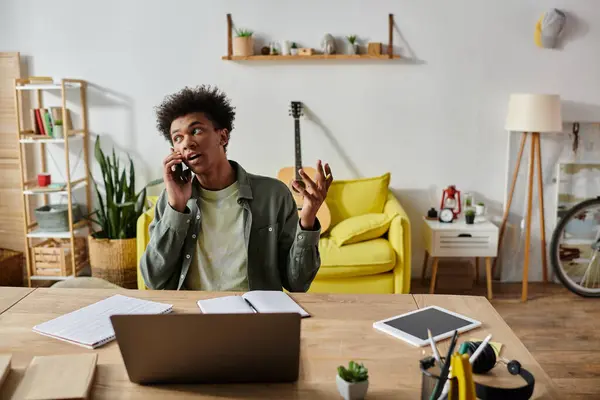A young African American man talks on the phone while studying online at home. — Stock Photo