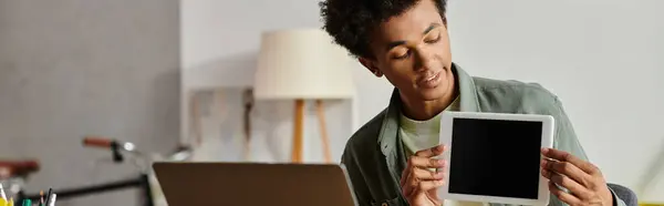 A man holds up a tablet in front of a laptop while studying online at home. — Stock Photo