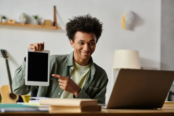 Young man of African American descent pointing at tablet device while studying online at home. — Foto stock