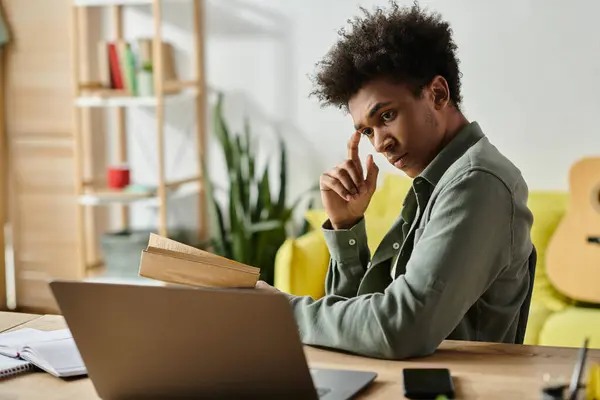 Young man engrossed in laptop and book at desk. — Foto stock