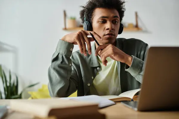 A young African American man is focused on his laptop, studying online while wearing headphones. - foto de stock