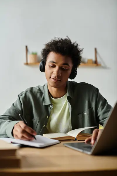 A young man immersed in online learning, sitting at a desk with headphones and a laptop. — Stockfoto