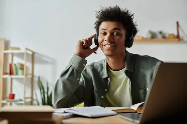 Young man with headphones studying with laptop and book at desk. — Stock Photo