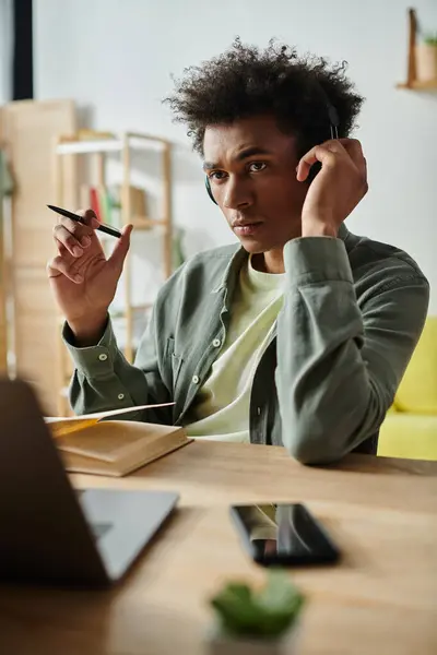 A young man of African American descent is focused on his laptop and wearing headphones while studying at a desk. — Stock Photo