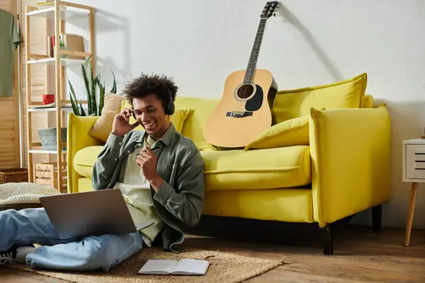 Young man, laptop, guitar, yellow couch. - foto de stock