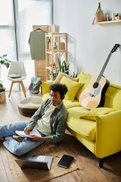 Young man, African American, sits near yellow couch with guitar. — Fotografia de Stock