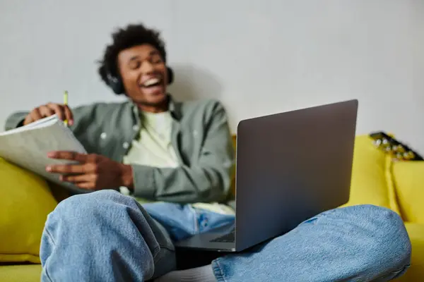 Young man studying with laptop on yellow couch and headphones. — Fotografia de Stock