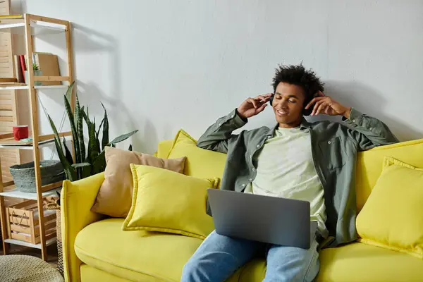 Young man with headphones sitting on yellow couch. — Stockfoto