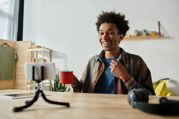 Young African American male blogger engages on phone whilst seated with a coffee cup. - foto de stock