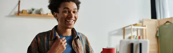 A young man smiles while holding a cup of coffee. — стокове фото