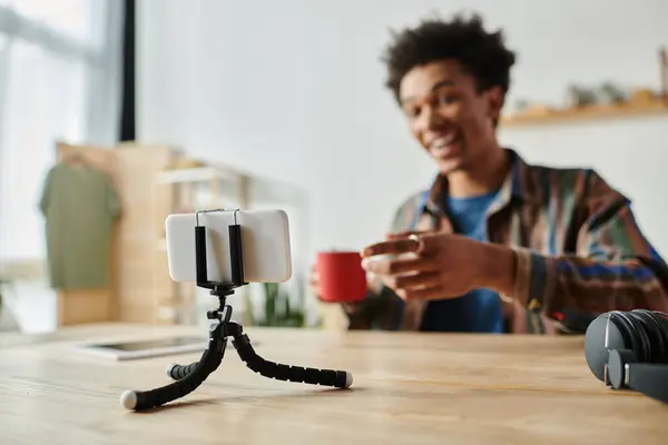 Young man sitting at table, recording video on phone tripod. — стоковое фото