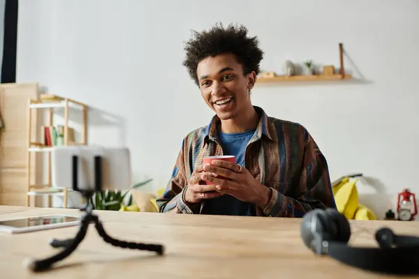 Young man, African American, blogs while sipping coffee and chatting on phone camera. — Stockfoto