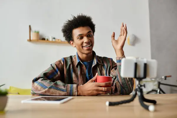 A young African American man sits at a table with a phone and a cup of coffee. — Foto stock