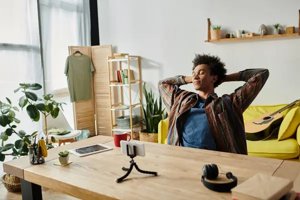 Young African American male blogger sitting at desk, hands on head, deep in thought. - foto de stock