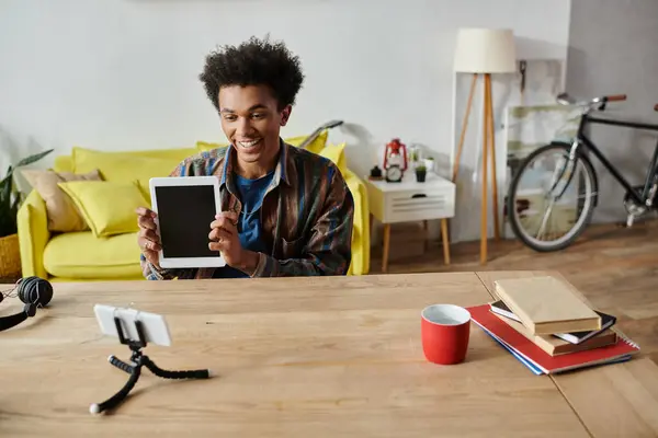 Young man, African American, holding tablet, in front of yellow table. — Foto stock
