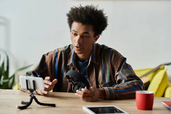 A young African American man sits at a table, engaging with a phone and tripod while talking. — Foto stock