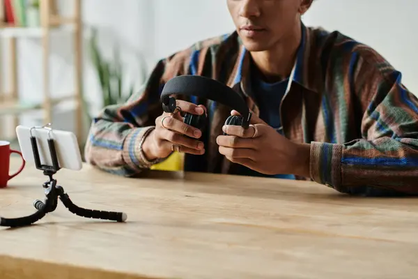 A young African American male blogger simultaneously holds a phone and a headset. — стокове фото