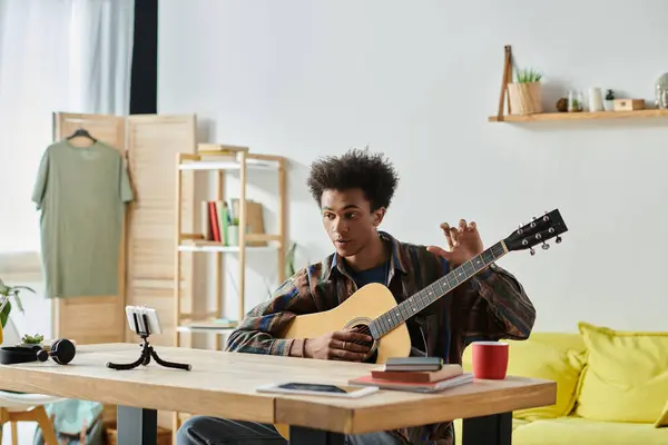 A young man, playing an acoustic guitar, creates music in his cozy living room. — Stock Photo