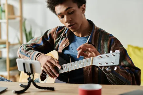 A man strums an acoustic guitar in front of a phone while live streaming. - foto de stock