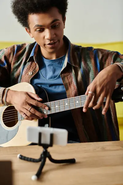 A young man creates beautiful music, playing an acoustic guitar in front of a phone. — Foto stock
