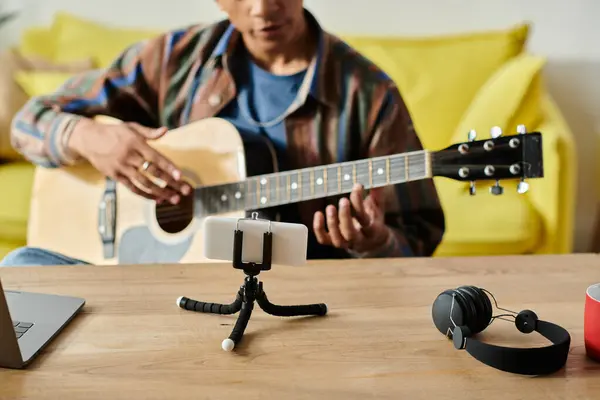 A young African American musician plays an acoustic guitar on a table while filming for his blog. — стоковое фото